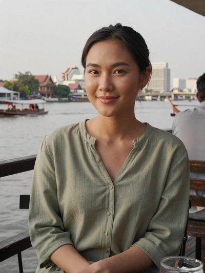 Kwanjai, 32, verified Thai woman in sage green blouse at a riverside cafe in Bangkok